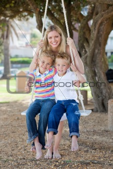 Smiling mother and her children swinging 