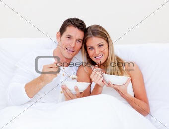 Romantic couple eating cereals lying in bed