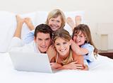 Smiling family looking at a laptop lying down on bed