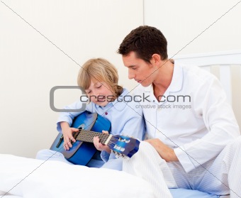 Adorable little boy playing guitar with his father