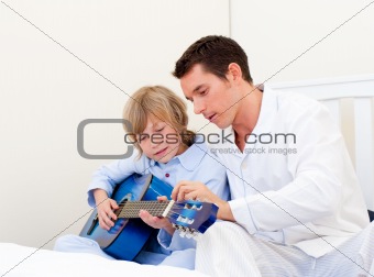 Cute little boy playing guitar with his father