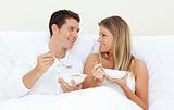 Affectionate couple having breakfast lying on their bed