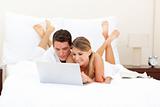 Happy couple surfing the internet lying on their bed