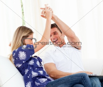 Mirthful couple using a laptop sitting on sofa