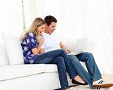 Cheerful couple using a laptop sitting on sofa