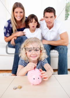 Smiling little girl inserting coin in a piggybank in the living room