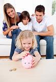 Adorable little girl inserting coin in a piggybank
