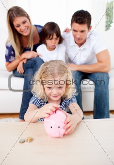 Adorable little girl inserting coin in a piggybank