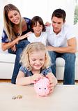 Smiling little girl inserting coin in a piggybank