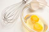Hand Mixer with Eggs in a Glass Bowl on a Reflective White Background.