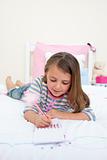 Concentrated Little girl writing on a notebook lying on her bed