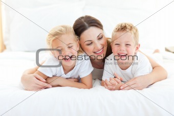 Happy siblings playing with their mother lying on a bed 