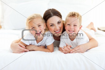 Laughing children playing with their mother lying on a bed