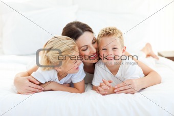 Cute children and their mom having fun lying on a bed 