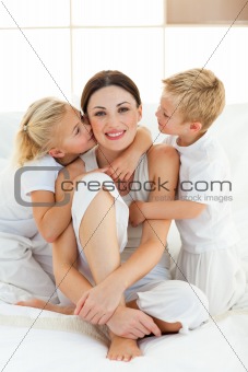 Children kissing their mother sitting on a bed