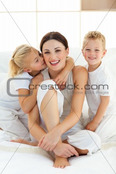 Cute children kissing their mother sitting on a bed 