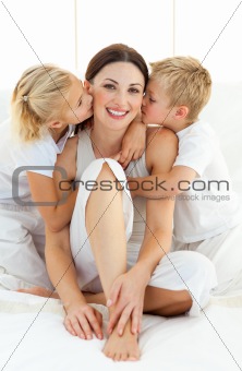 Adorable siblings kissing their mother sitting on a bed
