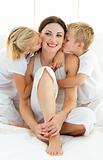 Jolly siblings kissing their mother sitting on a bed 