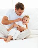 Happy father playing with his boy on a bed 