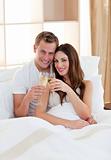 Affectionate couple drinking champagne lying in bed
