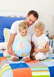 Blond siblings and their father looking at a terrestrial globe
