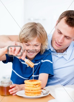 Jolly boy and his father putting honey on waffles