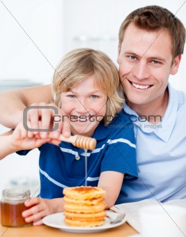 Happy boy and his father putting honey on waffles