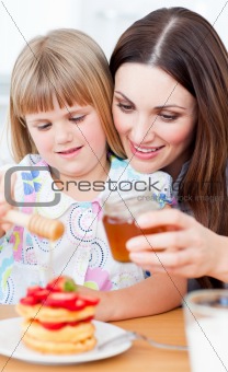 Joyful mother and her daughter putting honey on waffles