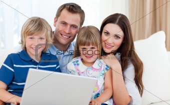 Jolly family using a laptop sitting on sofa