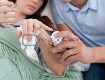 Close-up of a man giving pills to his wife lying on the sofa