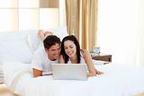 Happy couple using a laptop lying on their bed