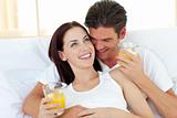 Young couple drinking orange juice lying on their bed 