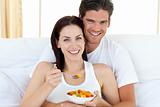 Happy couple eating fruits lying on their bed