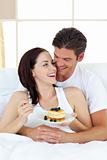 Joyful couple eating pancakes lying on their bed
