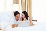 Young couple using a laptop lying on their bed 