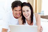 Smiling couple using a laptop lying on their bed 