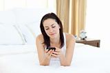 Attractive woman sending a text lying on her bed 