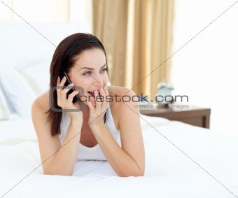 Surprised woman on phone lying on her bed 