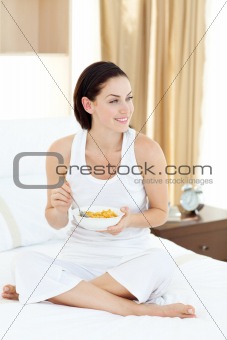 Jolly woman having breakfast sitting on her bed at home