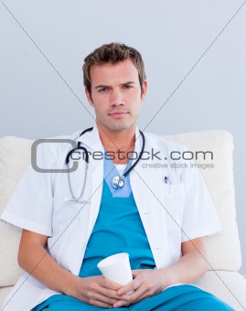 Serious male doctor drinking coffee