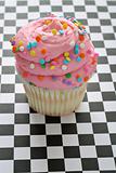 shot of pink sprinkle cupcake on checkered background