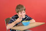shot of a young boy eating cereal at desk