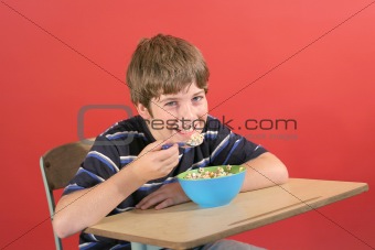 shot of a young boy eating cereal at desk