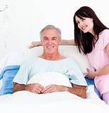 Smiling nurse fixing a senior patient's bed 
