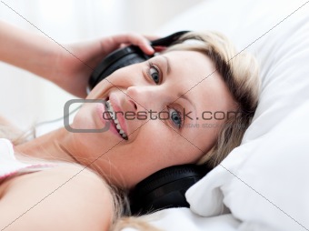 Positive woman with headphones on lying on a bed