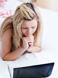 Concentrated woman using a laptop lying on her bed