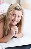 Smiling woman using a laptop lying on her bed 