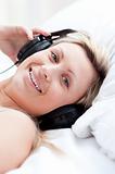 Positive woman with headphones on lying on her bed 