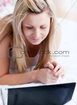 Serious woman using a laptop lying on a bed