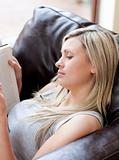 Concentrated woman reading a book sitting on a sofa